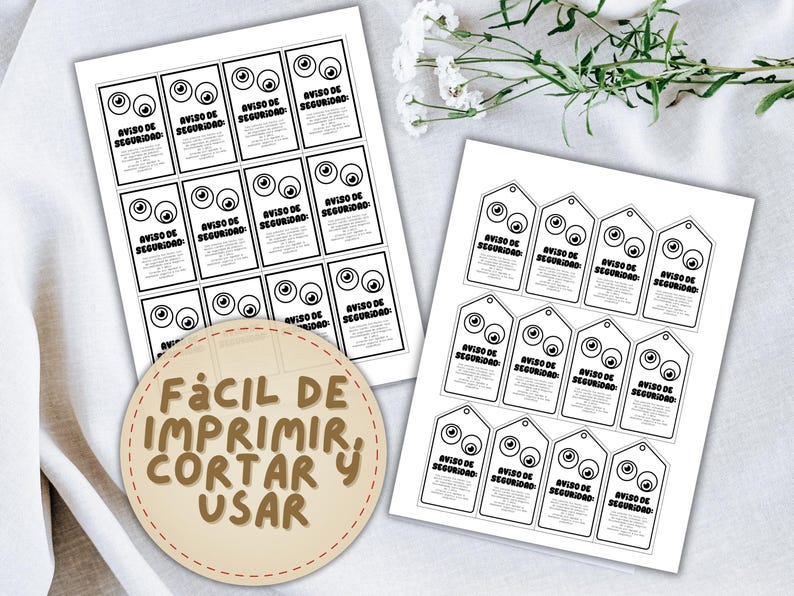 May include: Two sheets of printed paper with black text and eye graphics. One sheet has rectangular labels, the other has tag-shaped labels. The text on the labels reads "AVISO DE SEGURIDAD". A circular label says "F&Aacute;CIL DE IMPRIMIR, CORTAR Y USAR".