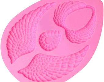 May include: Pink silicone mold with three angel wing shapes. The wings have a detailed textured design.