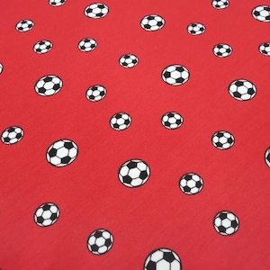 Puede incluir: Tela roja con un patrón repetido de balones de fútbol en blanco y negro. Los balones están dispersos por la superficie, creando un diseño deportivo y lúdico. La tela tiene una textura suave.