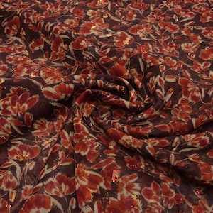 May include: Close-up of a fabric with a floral pattern. The fabric has a dark burgundy base with a repeating pattern of red and cream-coloured flowers. Gold metallic accents are scattered throughout the design, adding a touch of shimmer.