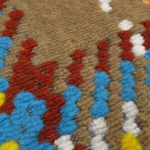 Puede incluir: Primer plano de una alfombra tejida con un patr&oacute;n geom&eacute;trico colorido. La alfombra presenta tonos de marr&oacute;n, azul, rojo, amarillo y blanco.