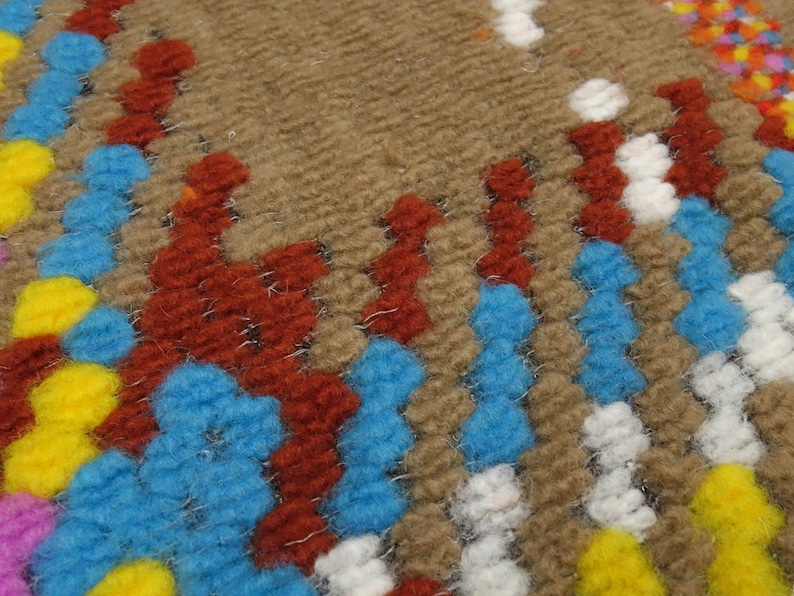 Puede incluir: Primer plano de una alfombra tejida con un patr&oacute;n geom&eacute;trico colorido. La alfombra presenta tonos de marr&oacute;n, azul, rojo, amarillo y blanco.