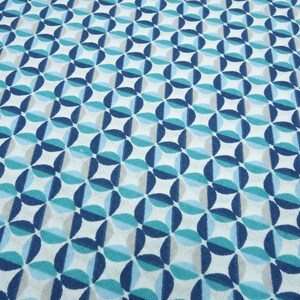 Könnte beinhalten: Ein weißer Stoff mit einem sich wiederholenden Muster aus blauen, türkisfarbenen und grauen Kreisen, die ein geometrisches Design bilden.