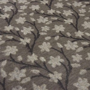 May include: A textile fabric featuring a dark brown background with a repeating pattern of dark charcoal branches and light beige five-petaled flowers. The material has a soft, slightly fuzzy texture with a visible woven knit construction throughout.