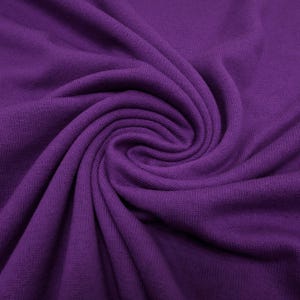 May include: Close-up of a swirl of deep purple fabric. The knit material has a textured appearance, with visible ridges and a soft, flowing drape. The fabric is tightly woven, creating a smooth surface with subtle variations in color.