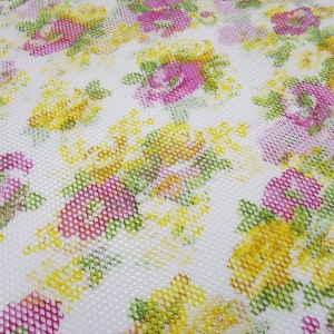 Könnte beinhalten: Weißer Stoff mit einem sich wiederholenden Muster aus rosa und gelben Blumen auf weißem Hintergrund. Der Stoff hat eine strukturierte, netzartige Optik.