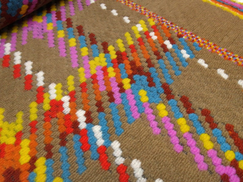 Puede incluir: Primer plano de una alfombra tejida marr&oacute;n con rayas de colores rosa, azul, amarillo, naranja y rojo. Las rayas est&aacute;n hechas de peque&ntilde;as bolas redondas y peludas.
