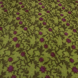 Pode incluir: Close-up de um tecido verde com um padrão repetido de folhas castanhas escuras e flores roxas. As flores são espaçadas uniformemente, criando um design floral texturizado.