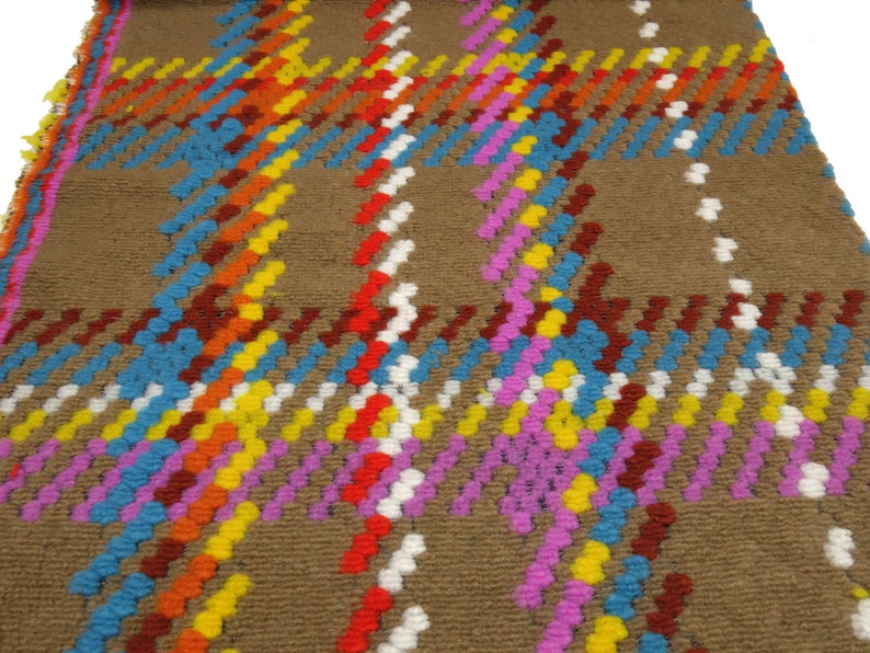 Puede incluir: Una alfombra marr&oacute;n con un patr&oacute;n de cuadros de colores. El patr&oacute;n est&aacute; formado por peque&ntilde;os bucles redondos tejidos en tonos de rojo, naranja, amarillo, azul, rosa y blanco.