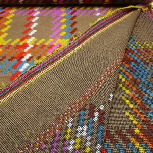 Puede incluir: Primer plano de una tela marr&oacute;n con un patr&oacute;n geom&eacute;trico colorido. La tela tiene una textura tejida y est&aacute; doblada por la mitad. El patr&oacute;n est&aacute; formado por cuadrados y rect&aacute;ngulos en tonos de rojo, naranja, amarillo, azul, verde y blanco.