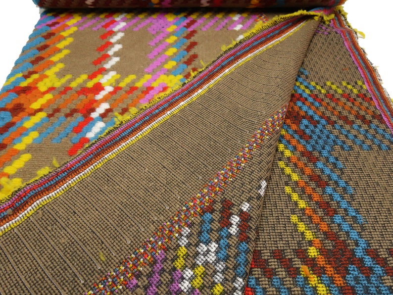 Puede incluir: Primer plano de una tela marr&oacute;n con un patr&oacute;n geom&eacute;trico colorido. La tela tiene una textura tejida y est&aacute; doblada por la mitad. El patr&oacute;n est&aacute; formado por cuadrados y rect&aacute;ngulos en tonos de rojo, naranja, amarillo, azul, verde y blanco.