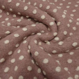 May include: Close-up of a dusty rose fabric with a pattern of raised, off-white polka dots. The fabric is soft and textured, with visible folds and shadows, creating a sense of depth and dimension. The polka dots are evenly spaced.