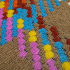 Puede incluir: Primer plano de una alfombra tejida con un patr&oacute;n geom&eacute;trico en tonos marrones, azules, rosas, amarillos y naranjas.