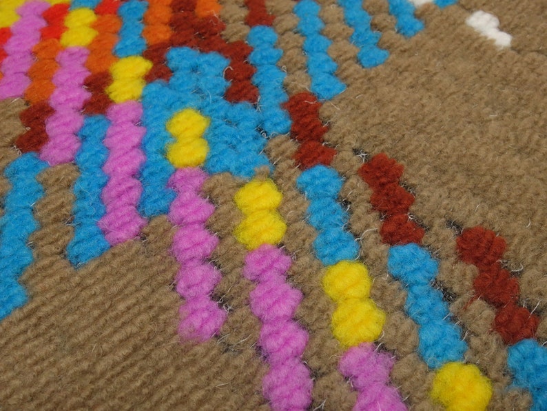 Puede incluir: Primer plano de una alfombra tejida con un patr&oacute;n geom&eacute;trico en tonos marrones, azules, rosas, amarillos y naranjas.