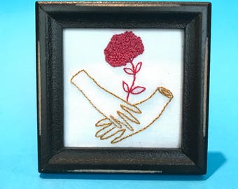 Hands holding french knot flowers, Framed hand-embroidered illustration