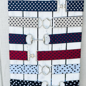May include: Six different patterned belts with silver buckles. The belts are displayed on a white wooden background. The patterns include polka dots in various colors, including navy blue, beige, red, burgundy, light blue, and black.
