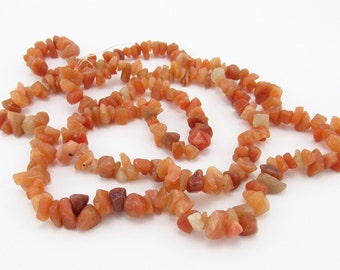 May include: A strand of orange carnelian chip beads. The beads are irregular in shape and have a natural, rough texture.