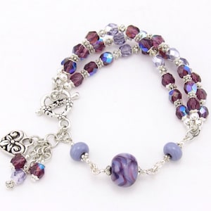 May include: A double-strand bracelet with purple and silver beads, a silver heart charm, and a large purple swirl bead.