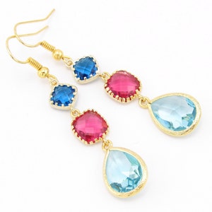 May include: Gold dangle earrings with three gemstone drops. The top two drops are square and red and blue. The bottom drop is teardrop shaped and light blue.