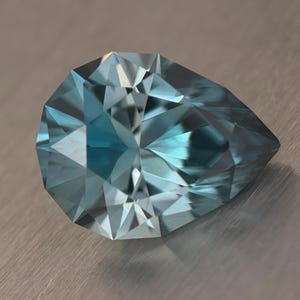 Puede incluir: Una gema facetada en forma de pera, de color azul claro. La superficie de la gema refleja la luz, mostrando sus m&uacute;ltiples facetas y su estructura interna. La gema se encuentra sobre un fondo met&aacute;lico neutro.