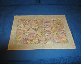 May include: A patchwork quilt with a floral pattern in shades of pink, green, and blue. The quilt is edged with a cream-colored border.