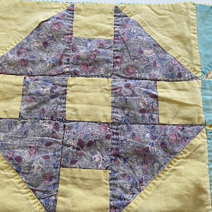 May include: A quilt block with a yellow and blue floral pattern. The block is made up of nine squares, with the center square being yellow and the surrounding squares being blue with a floral pattern.