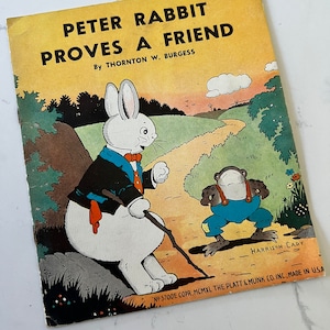 May include: A vintage children's book cover featuring Peter Rabbit, a white rabbit wearing a black suit and red scarf, sitting on a rock with a stick in his hand.  He is looking at a frog wearing overalls and a blue shirt. The book title is "Peter Rabbit Proves a Friend" by Thornton W. Burgess. The cover is yellow with green and brown illustrations.