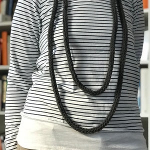 Peut inclure: Un long collier en corde tressée gris porté sur une chemise à manches longues rayée blanc et noir.