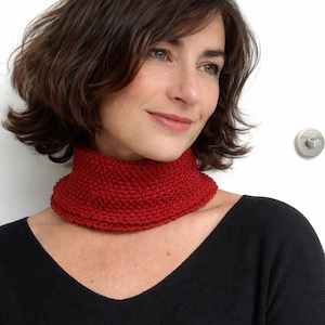 May include: A knitted red neck warmer. The neck warmer is a vibrant shade of red and has a textured appearance. The item is worn around the neck and is made of a soft, warm material. The neck warmer is a winter accessory.