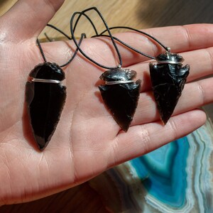 May include: Three black obsidian arrowhead pendants on black cords. Each pendant is wrapped with a silver wire.