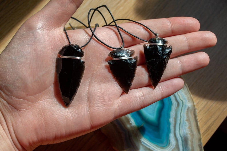 May include: Three black obsidian arrowhead pendants on black cords. Each pendant is wrapped with a silver wire.