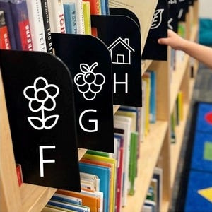 May include: Black shelf dividers for a wooden bookcase, each featuring a white line-art icon and a corresponding letter. The visible dividers display a flower with the letter F, a bunch of grapes with G, a house with H, and a leaf icon.