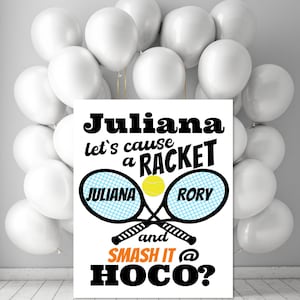 Puede incluir: Un letrero blanco con el texto "Juliana let's cause a RACKET" y "SMASH IT @ HOCO?" en negro y naranja. Dos raquetas de tenis con los nombres "Juliana" y "Rory" cruzadas. Globos blancos en el fondo.