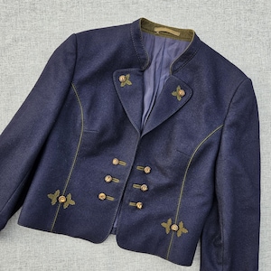 Può includere: Un blazer blu scuro con colletto alla coreana e bordo verde oliva, maniche lunghe e chiusura frontale con sei piccoli bottoni rotondi. La giacca è decorata con dettagli ricamati a forma di foglia color verde oliva vicino ai bottoni.