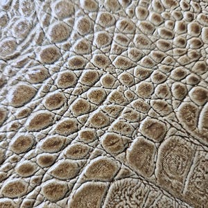 May include: Close-up of a textured surface with a pattern resembling crocodile skin. The color is a blend of light brown and tan, with darker brown accents in the crevices, creating a realistic effect. The surface has a bumpy, scaled texture.