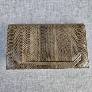 Könnte beinhalten: Eine rechteckige Clutch mit einer strukturierten Oberfläche in braunem und grauem Schlangenledermuster. Die Frontklappe ist mit einer horizontalen, abgewinkelten, goldfarbenen Metallleiste verziert, die den unteren Teil der Tasche überspannt.