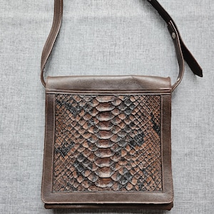 Puede incluir: Bolso de hombro de cuero marrón con un diseño de piel de serpiente en la solapa delantera. El bolso tiene una correa ajustable y una forma rectangular. El diseño de piel de serpiente presenta tonos marrones, negros y beige.