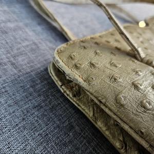May include: A beige shoulder bag with a textured, quill-patterned surface. The bag features a scalloped top edge, thin shoulder straps, and visible wear along the side seams, showing signs of material degradation and fraying on the edges.