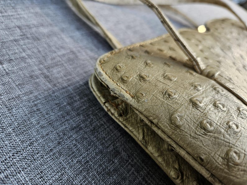 May include: A beige shoulder bag with a textured, quill-patterned surface. The bag features a scalloped top edge, thin shoulder straps, and visible wear along the side seams, showing signs of material degradation and fraying on the edges.