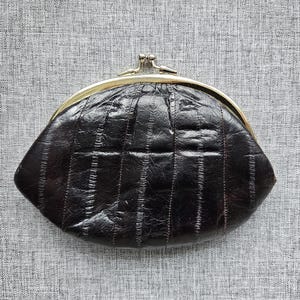 May include: A dark brown coin purse with a textured, segmented surface and a gold-toned metal kiss-lock clasp. The purse has a rounded, semi-circular shape and features a glossy finish with visible vertical lines across the material.
