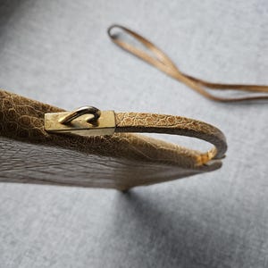 May include: A vintage beige handbag with a textured, crocodile-like pattern. The bag features a gold-coloured clasp and handle, with a matching strap. The bag is a classic accessory.