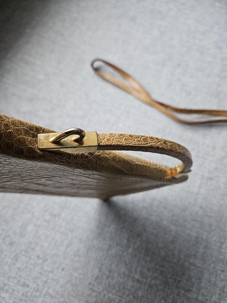 May include: A vintage beige handbag with a textured, crocodile-like pattern. The bag features a gold-coloured clasp and handle, with a matching strap. The bag is a classic accessory.