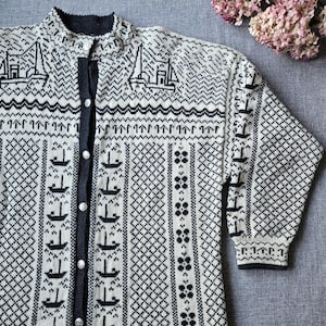 Può includere: Cardigan color crema con un motivo nautico nero con barche a vela e disegni geometrici. Il maglione con bottoni ha un collo alto e maniche lunghe. Il design include una serie di piccole barche e motivi a rombi. Il cardigan è lungo circa 71 cm.