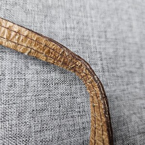 May include: Close-up of a section of a brown leather strap. The strap has a textured, patterned surface with visible stitching along the edges. The leather appears worn, with some areas showing signs of wear and tear.