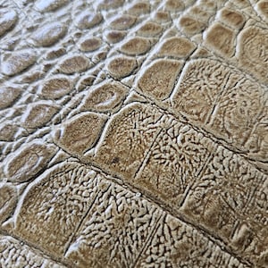 May include: Close-up of a textured surface with a pattern resembling crocodile skin. The colour is a blend of light and dark browns, with a slightly glossy finish. The design features a scale-like texture.