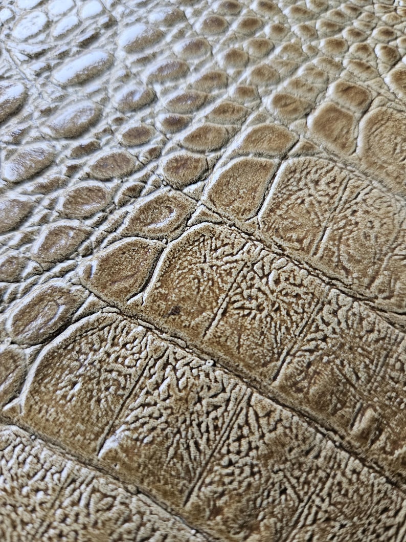 May include: Close-up of a textured surface with a pattern resembling crocodile skin. The colour is a blend of light and dark browns, with a slightly glossy finish. The design features a scale-like texture.