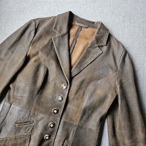 May include: A brown leather blazer with a classic design. The blazer has a notched collar, button closure, and two front pockets. The leather has a distressed appearance, with variations in colour and texture.
