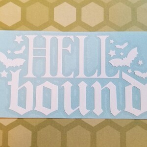 May include: A white vinyl decal on a light blue background. The decal features the words "HELL BOUND" in a gothic font, with bats and stars as decorative elements. The background is a light blue rectangle.