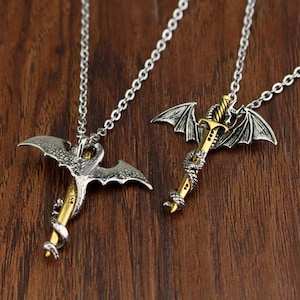 May include: Two silver necklaces with dragon and sword pendants. The dragon is wrapped around the sword, which is gold in color.