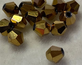 May include: A group of 12 gold-toned faceted glass beads. The beads are shaped like a pyramid with a pointed top and a flat base.